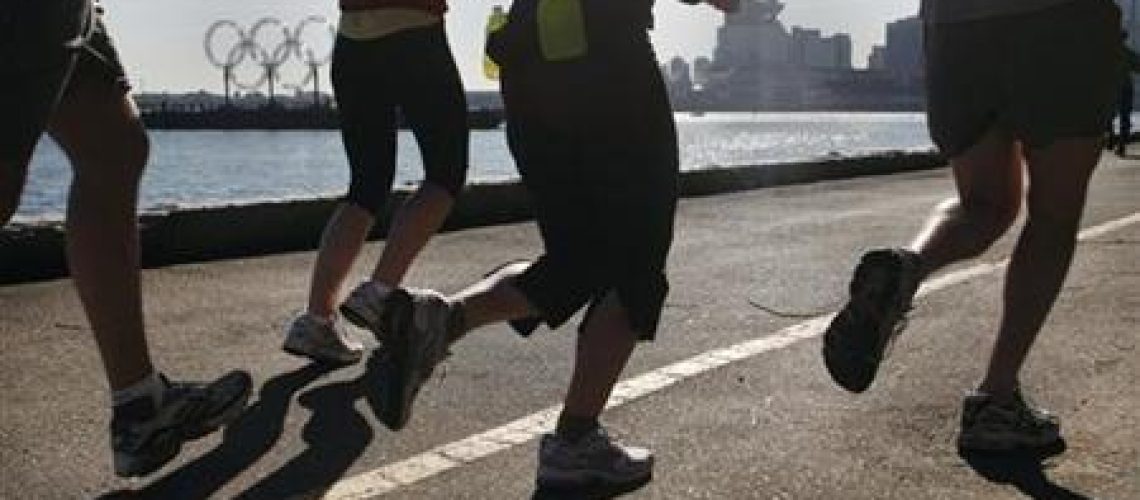 Joggers run along Stanley Park's seawall past the Olympic rings in Vancouver